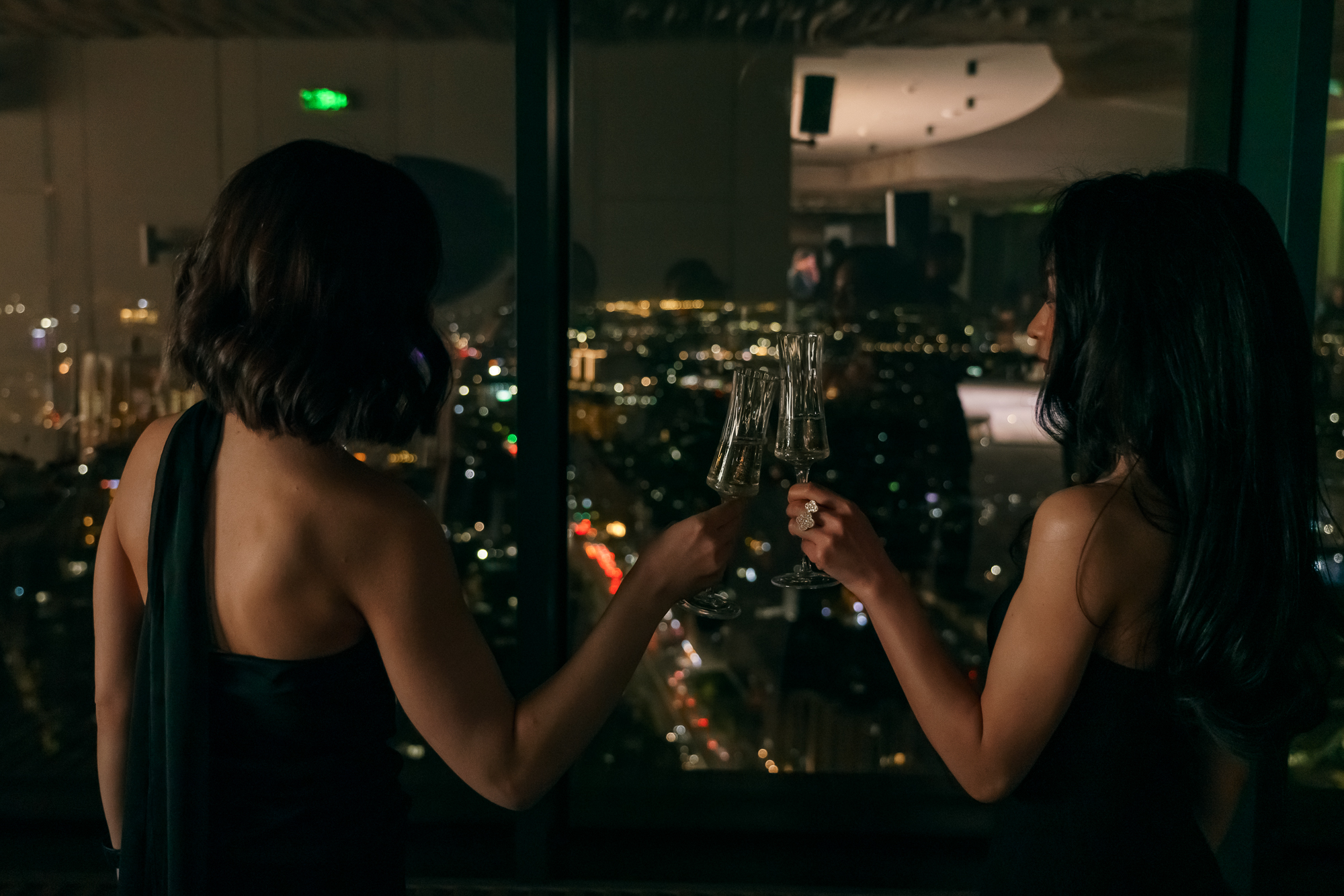 Rooftop Hall celebration — two guests in evening dresses toasting with champagne flutes against the panoramic night skyline of Tashkent