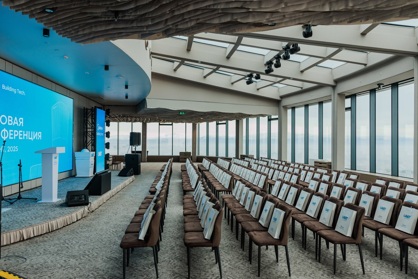 Conference at Rooftop Hall — theatre seating with stage and LED screens, floor-to-ceiling windows, 48th floor