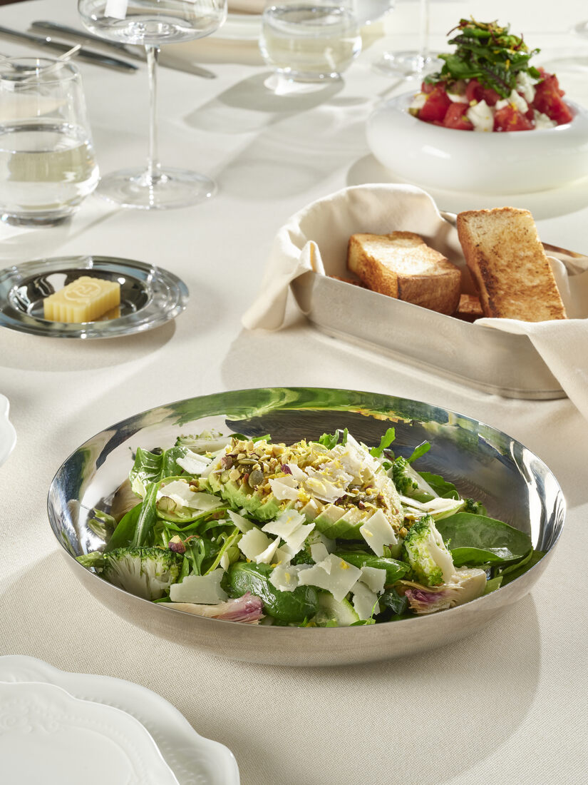 Green salad with parmesan in a silver serving bowl — table setting visible